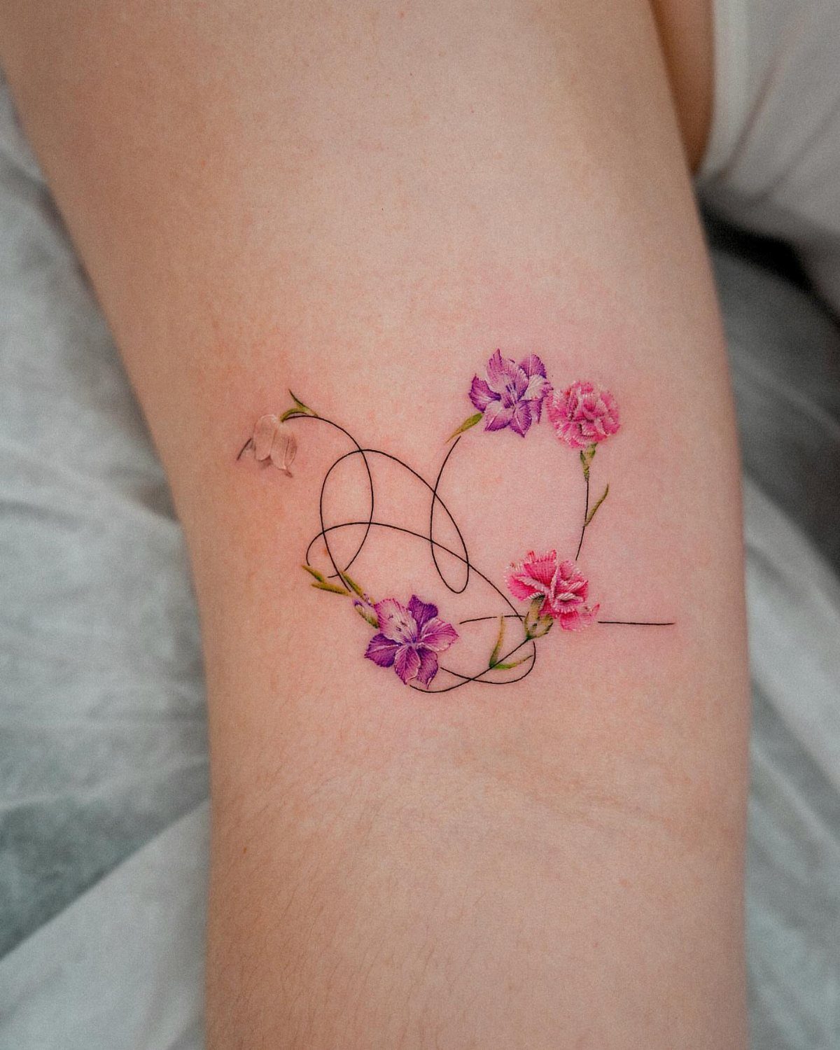 Heart-shaped tattoo with pink and purple flowers on a person's skin.