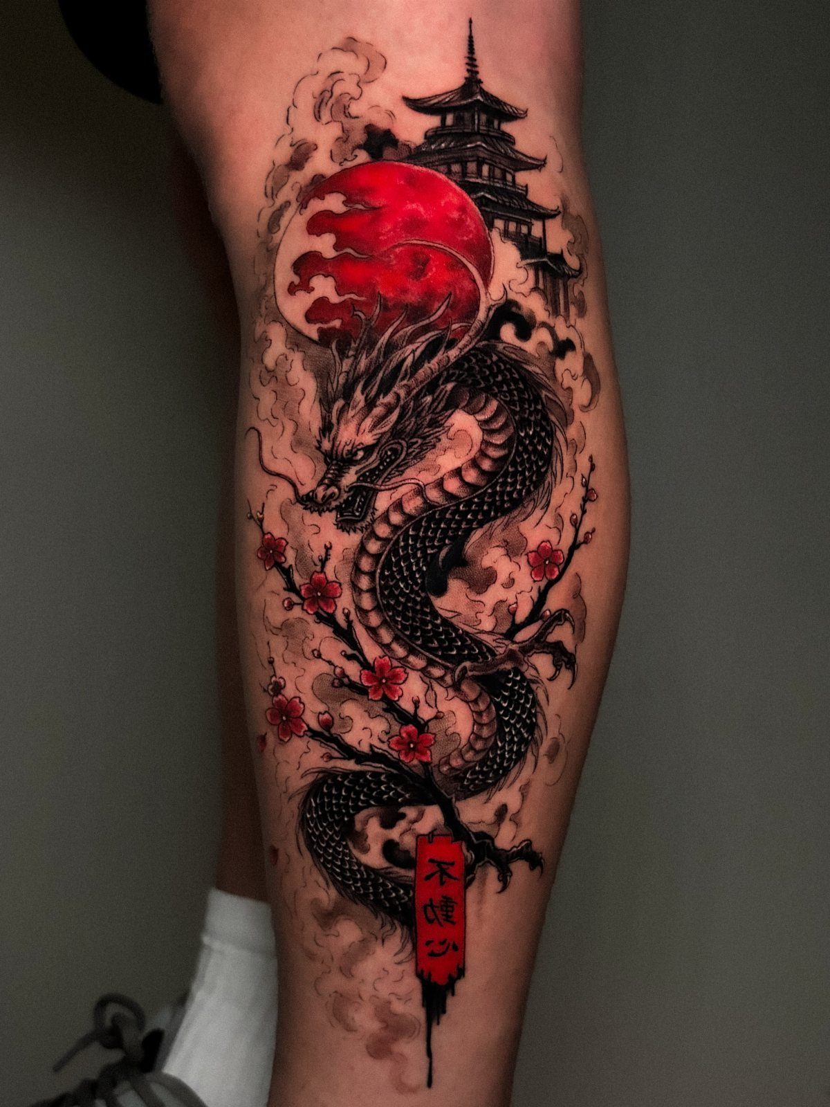 Asian dragon tattoo on a leg with red sun and pagoda silhouette