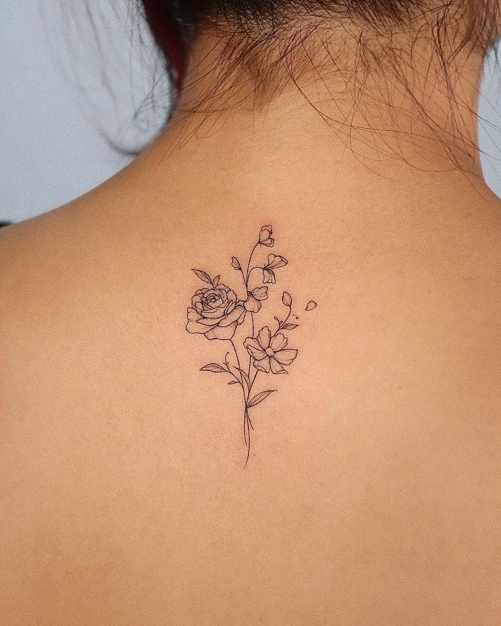 Floral bouquet tattoo with fine black lines on a person's upper back.