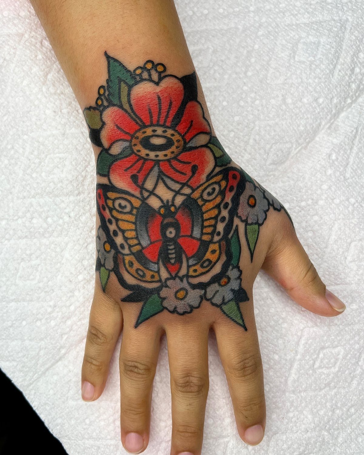 Colorful butterfly and flower tattoo on the back of a person's hand