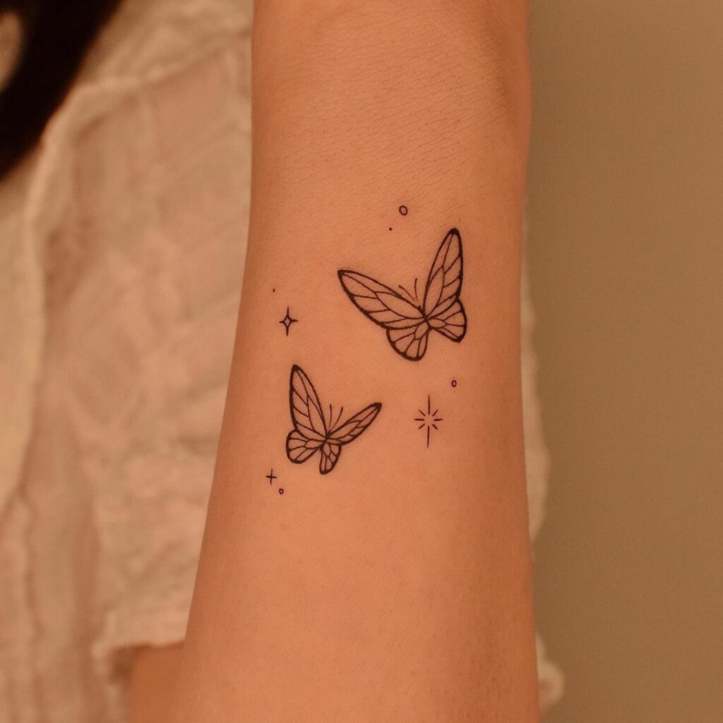 Two minimalist black ink butterfly tattoos with small stars on a forearm.