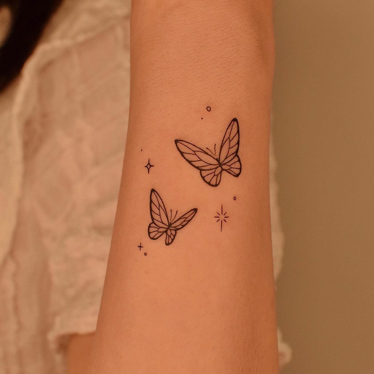 Two minimalist black ink butterfly tattoos with small stars on a forearm.