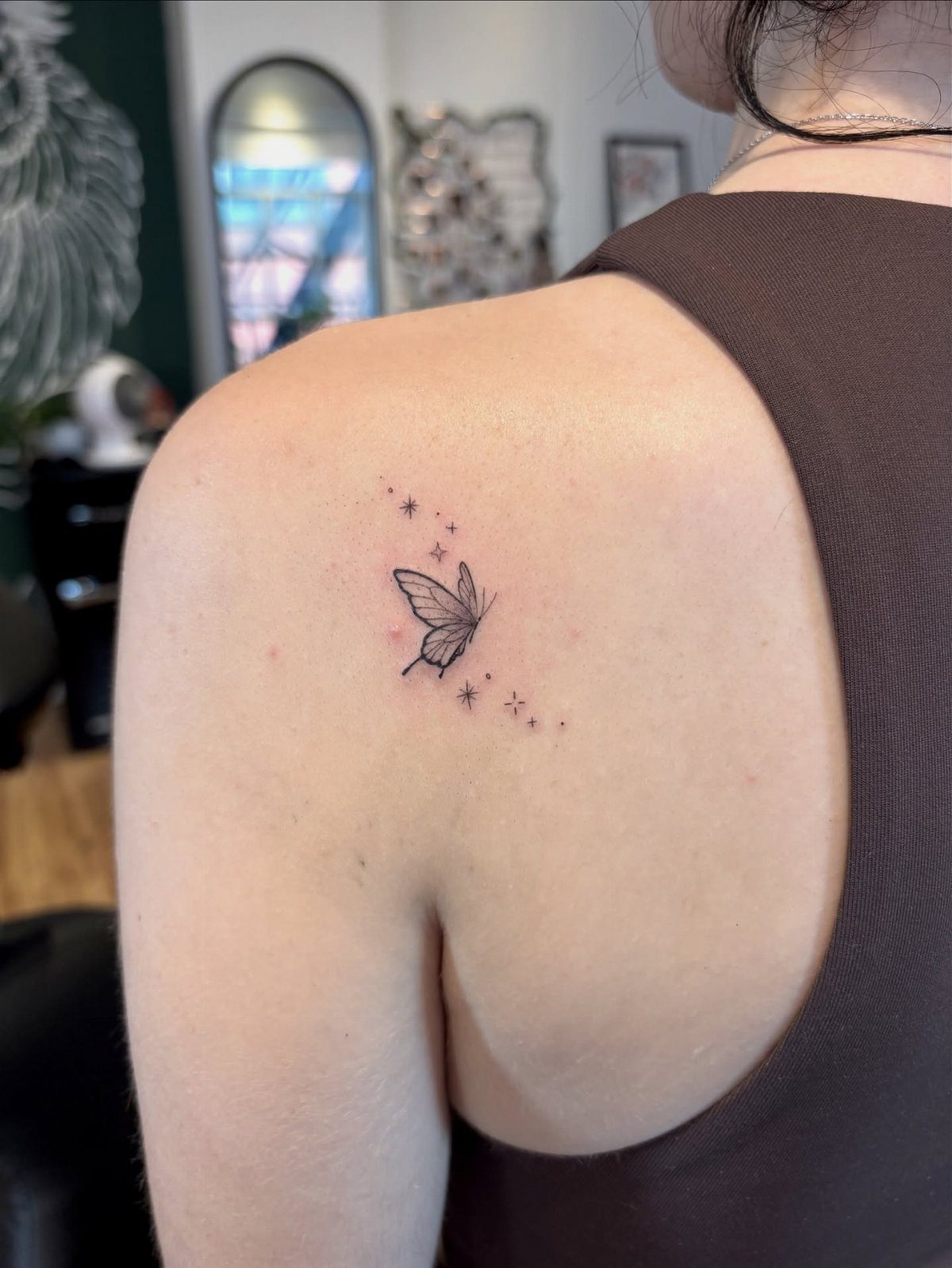 Small black butterfly tattoo with stars on a person's upper shoulder
