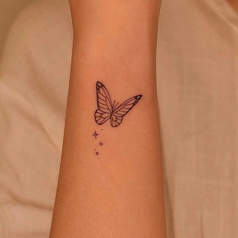 Small black ink butterfly tattoo with tiny stars on a person's forearm