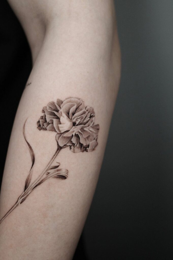 Carnation flower tattoo in black and grey ink on a person's forearm