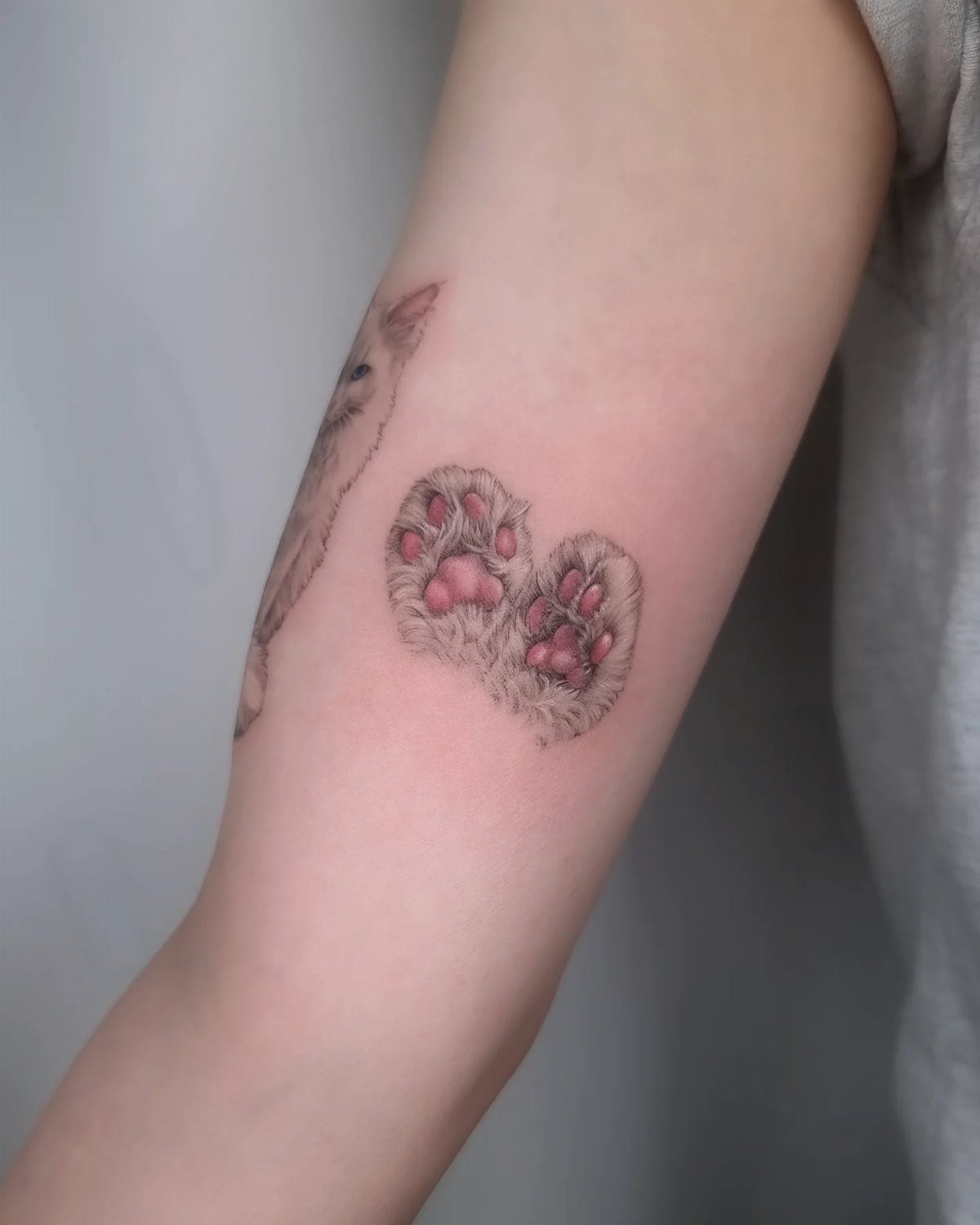Two realistic cat paw tattoos with pink pads on a person's forearm.