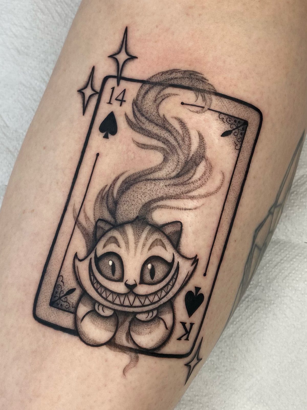 Cheshire Cat tattoo inside a playing card frame on a person's skin