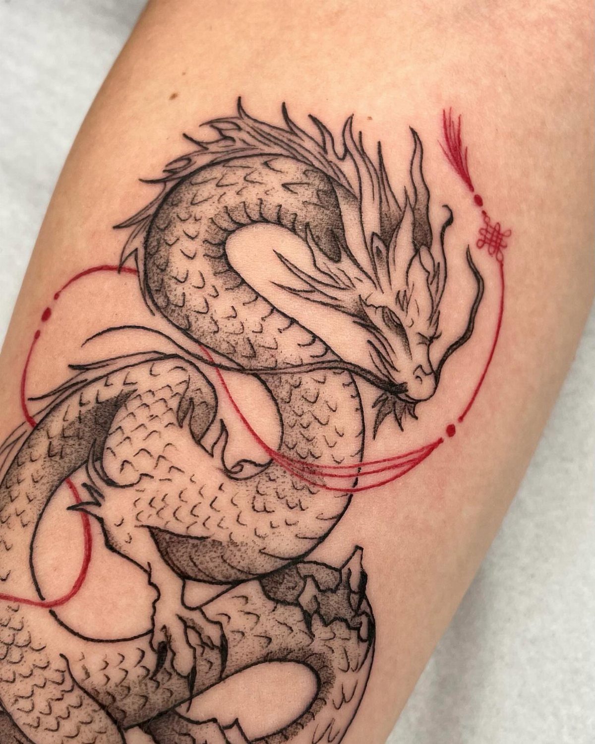 Chinese dragon tattoo with black ink and red accents on a person's arm