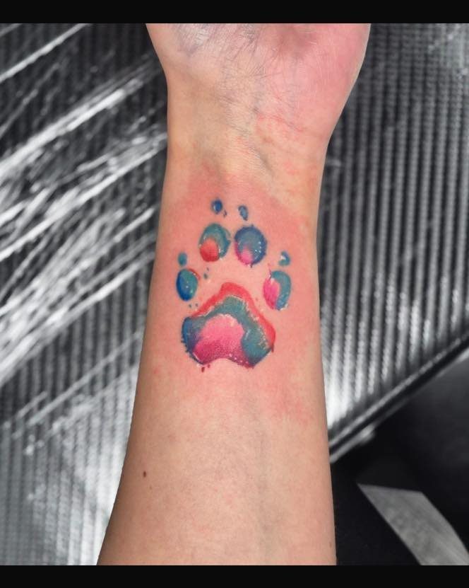 Watercolor dog paw print tattoo in blue and pink on a wrist