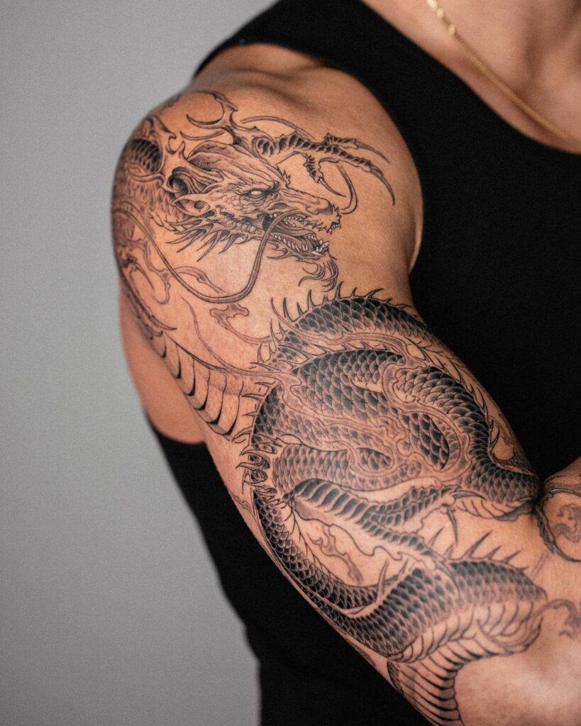 Detailed black and grey dragon tattoo covering a person's shoulder and upper arm.