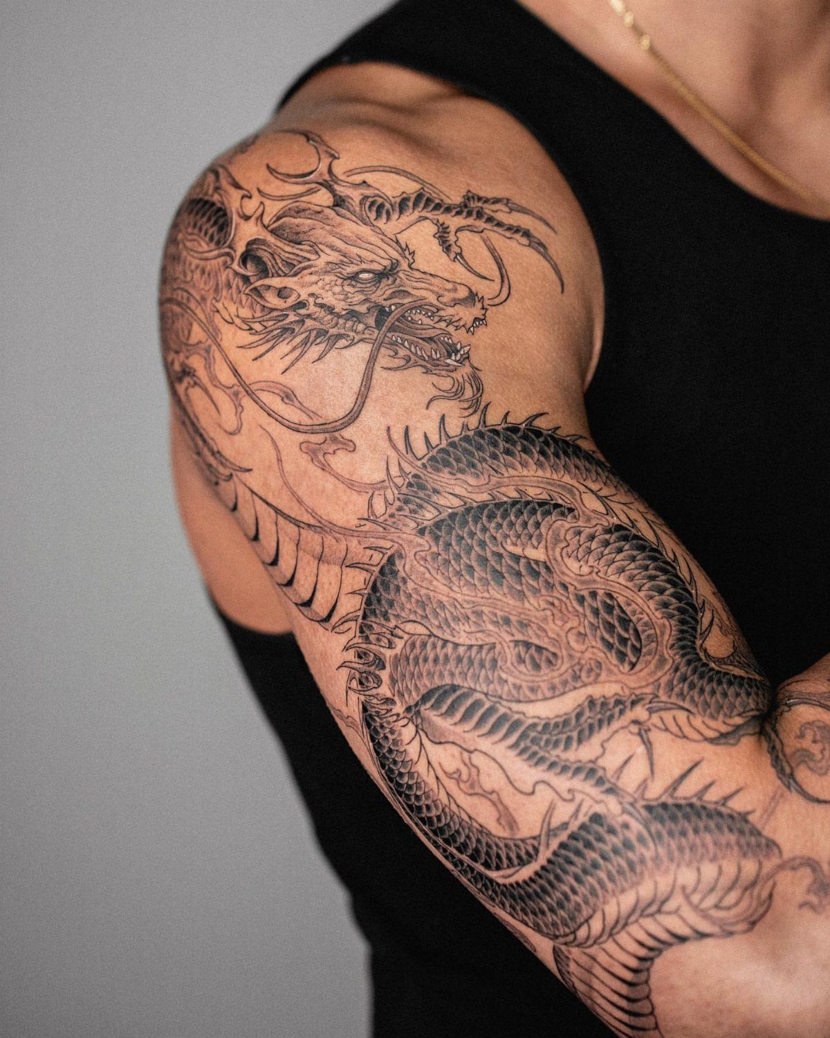 Detailed black and grey dragon tattoo covering a person's shoulder and upper arm.