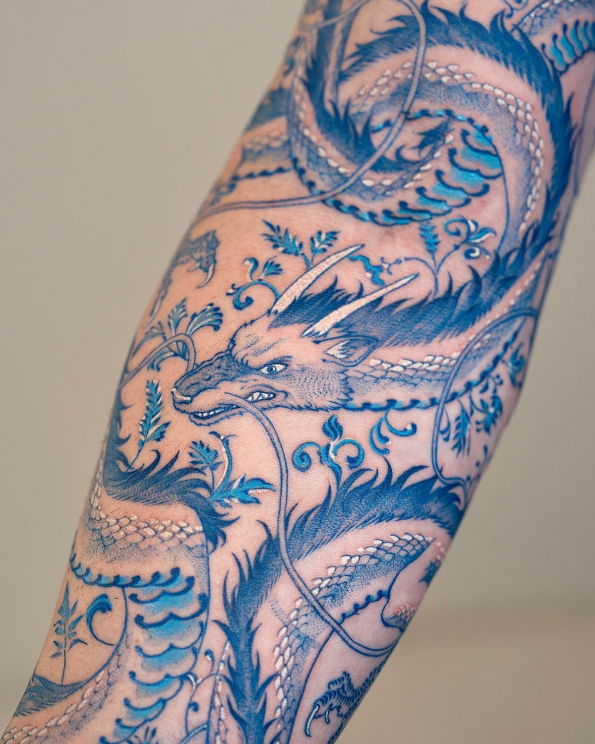 Blue dragon tattoo with intricate scales and waves on a person's arm