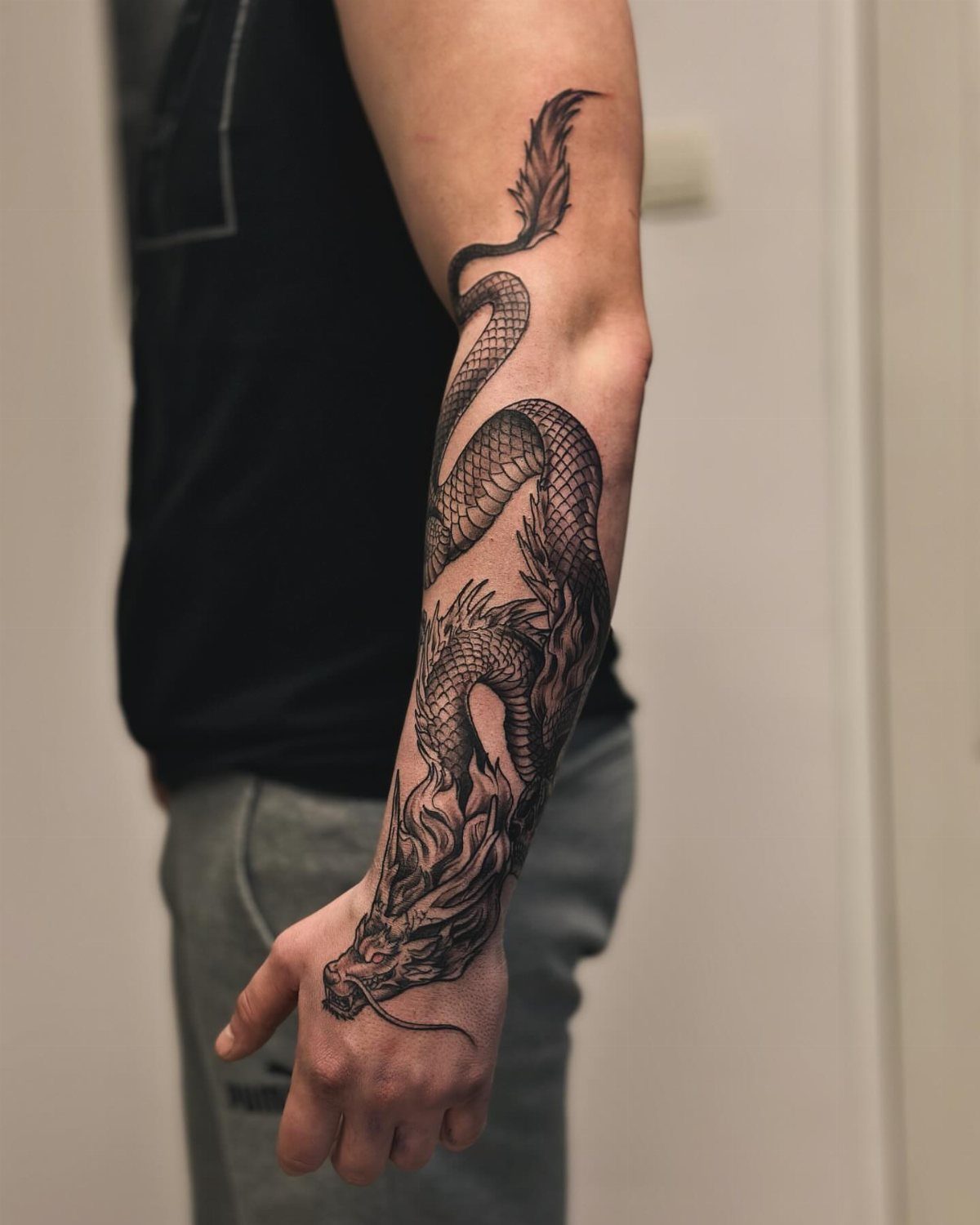 Black ink dragon tattoo wrapping around a man's forearm and wrist