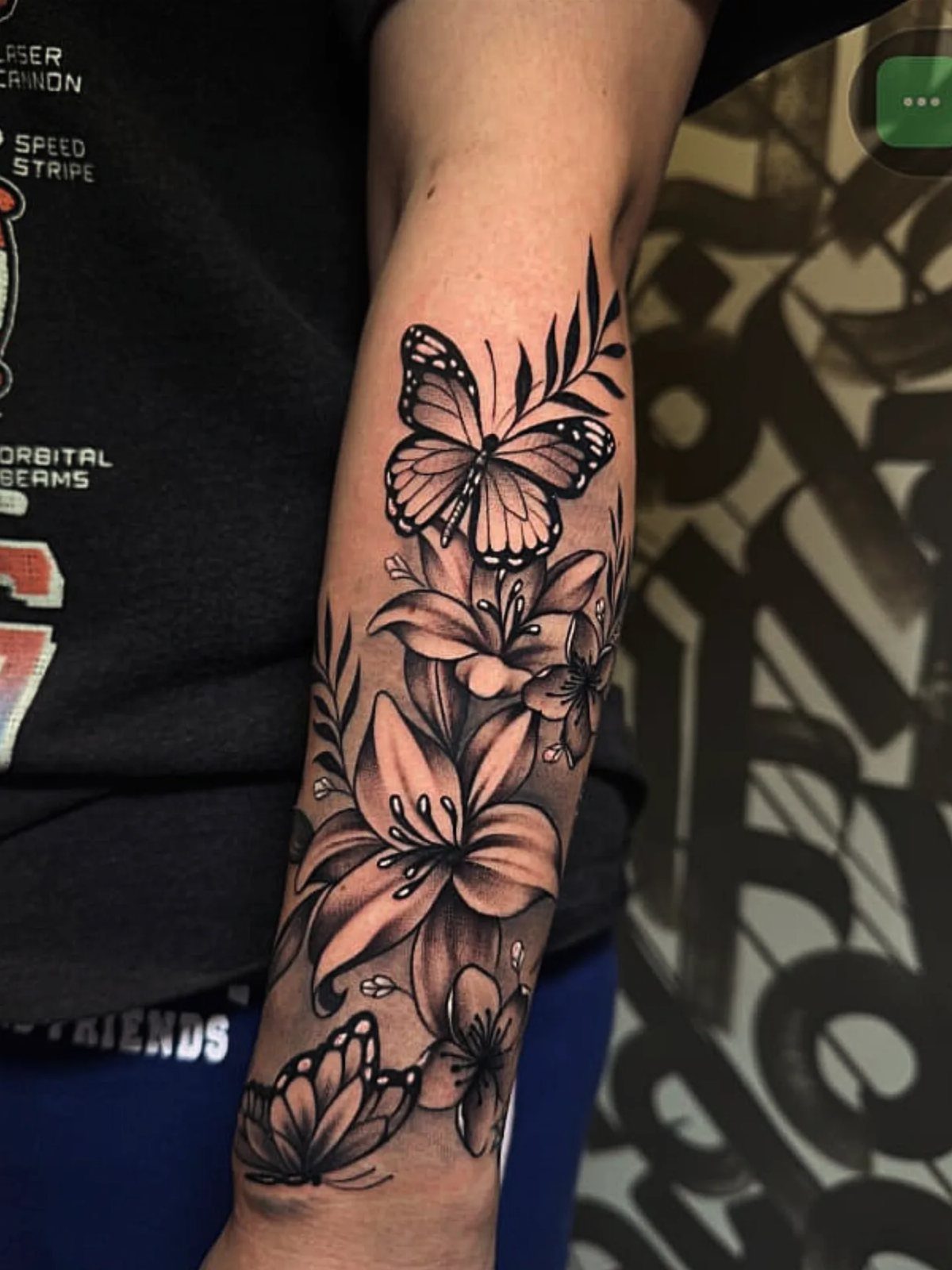 Black and grey tattoo of lilies and butterflies on a person's forearm