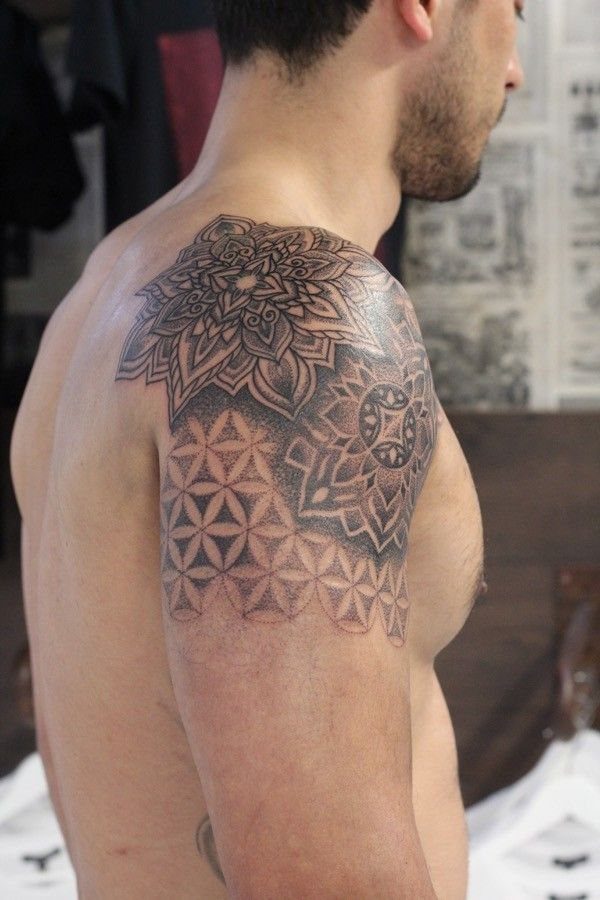 Man's shoulder with a black ink mandala and flower of life tattoo.