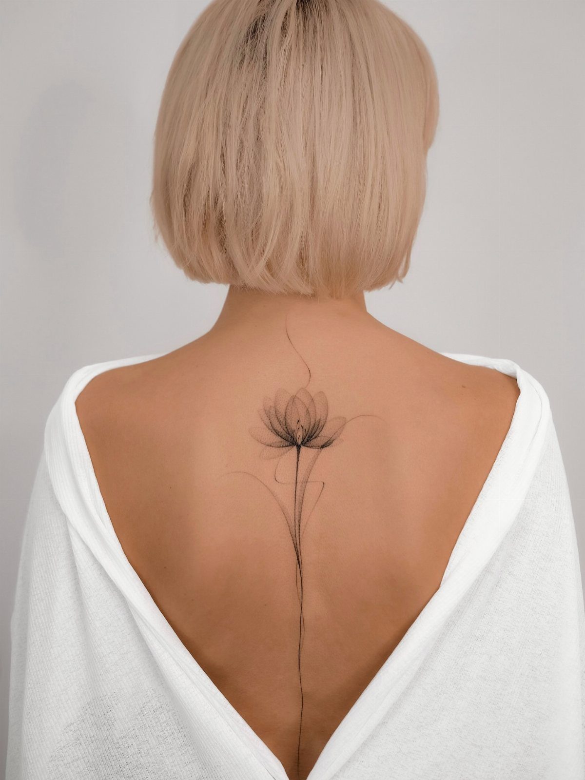 Fine-line flower tattoo with a long stem running down a person's spine.