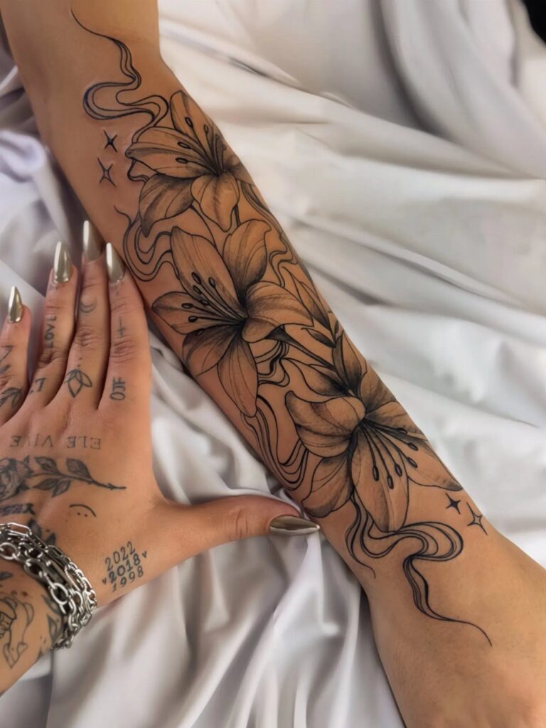 Large black ink lily flower tattoo covering a person's forearm on white fabric