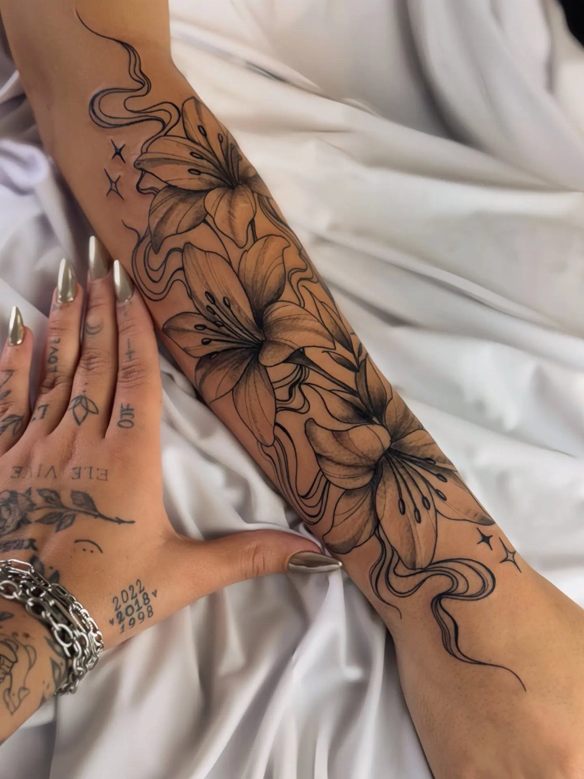 Large black ink lily flower tattoo covering a person's forearm on white fabric