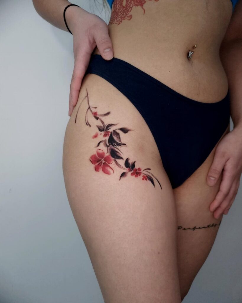 Red flower tattoo with black leaves on a person's hip and upper thigh