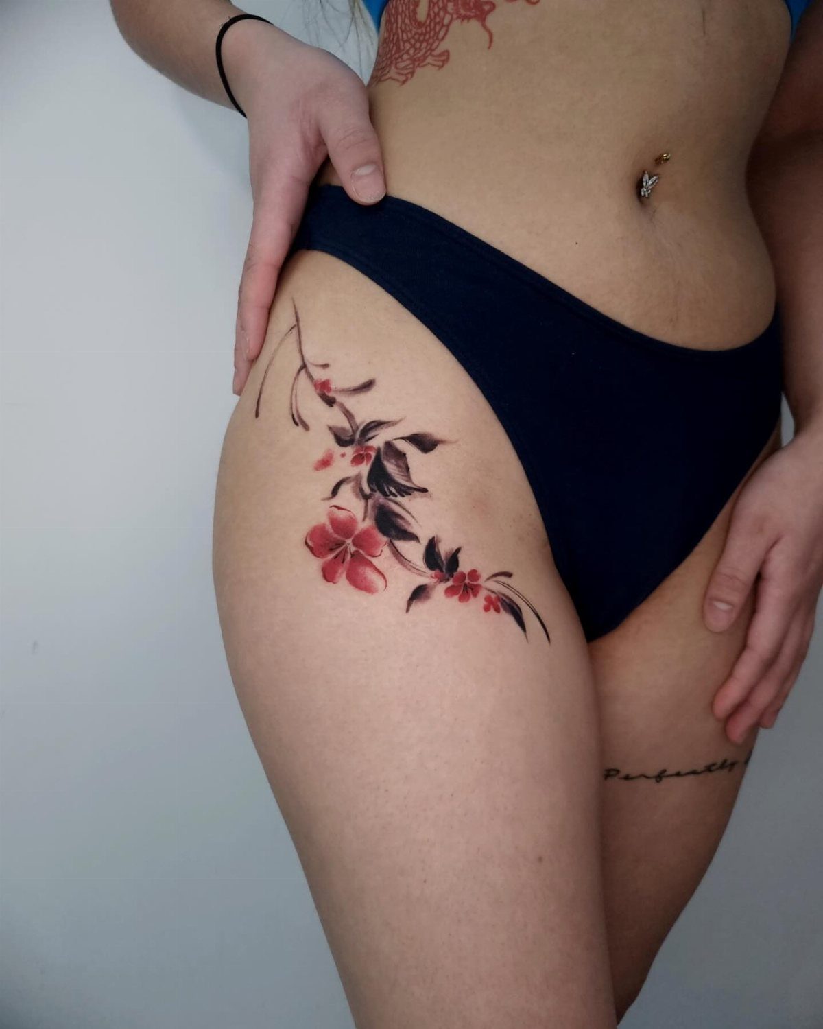 Red flower tattoo with black leaves on a person's hip and upper thigh
