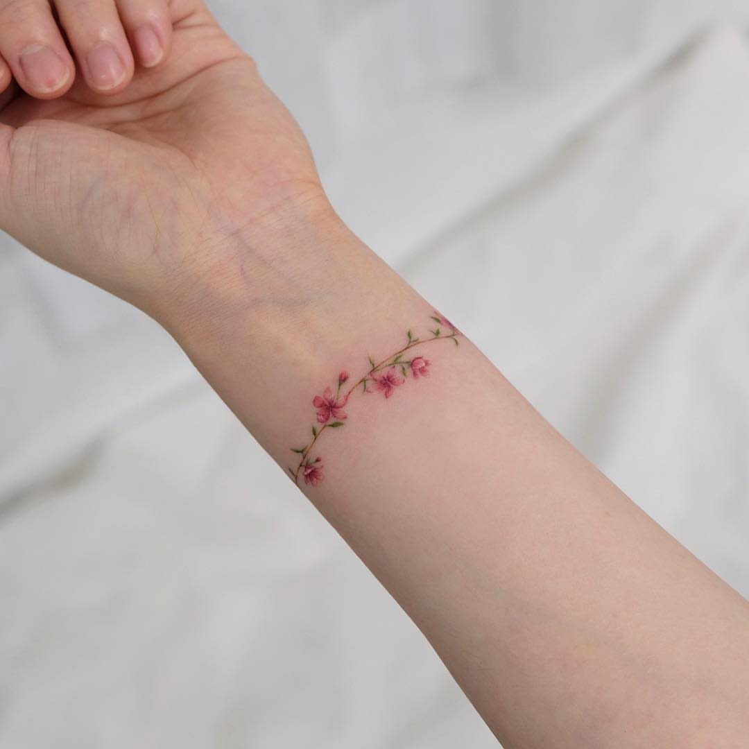 Delicate pink flower vine tattoo on a person's inner wrist against white fabric