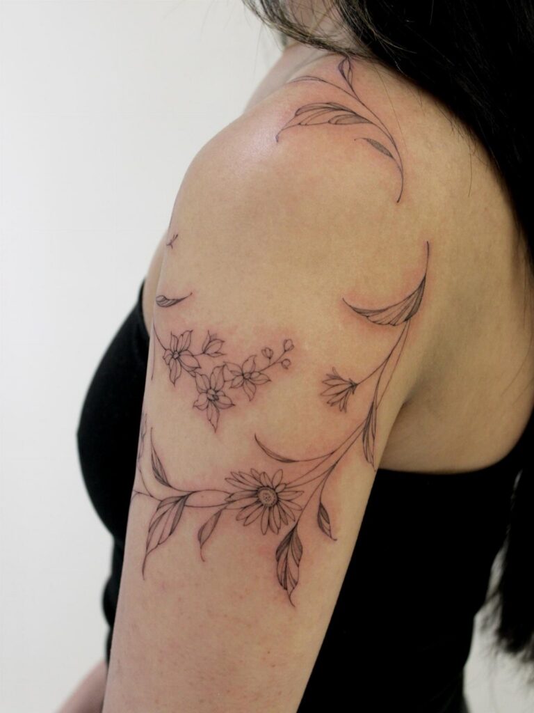 Floral tattoo with vines and leaves on a person's upper arm and shoulder