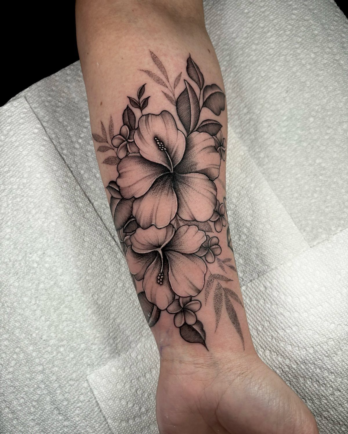 Hibiscus flower tattoo in black and grey ink on a person's forearm