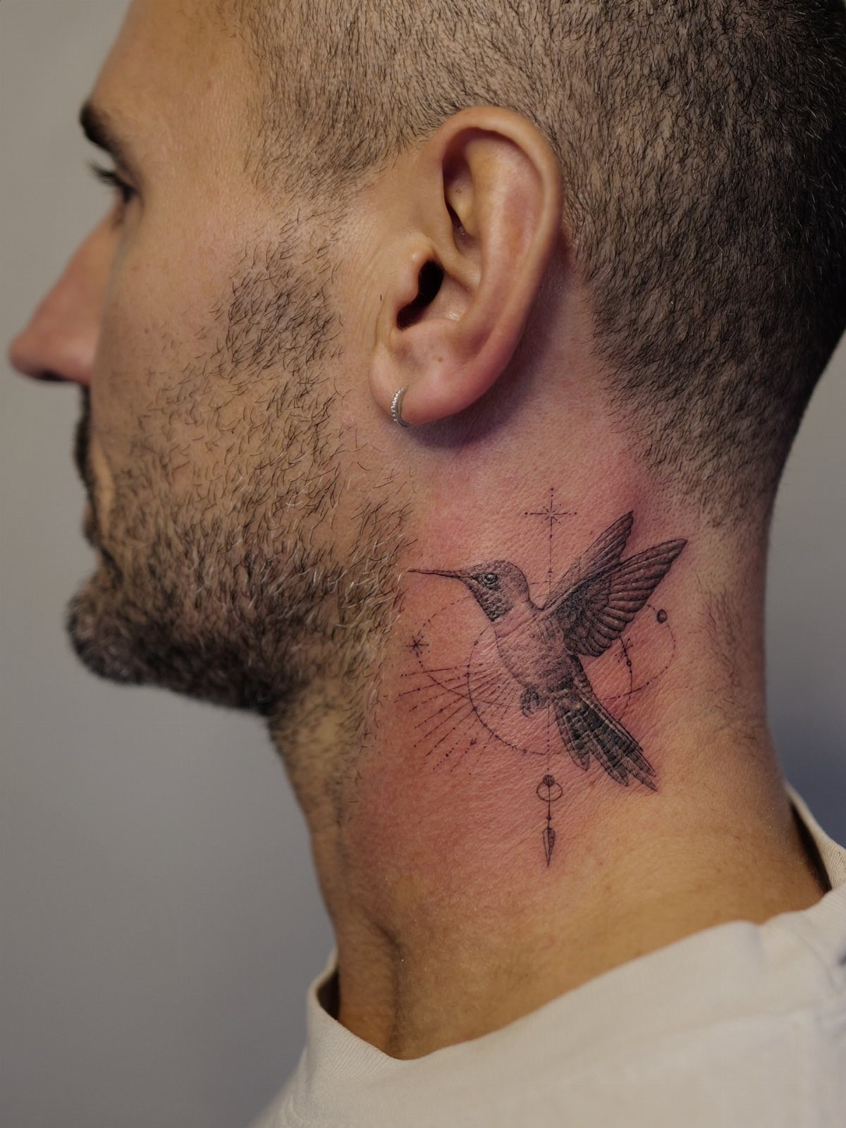 Hummingbird tattoo with geometric elements on a man's neck in profile view