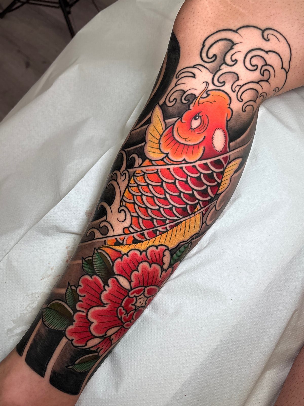 Orange koi fish tattoo with red peony and waves on a forearm