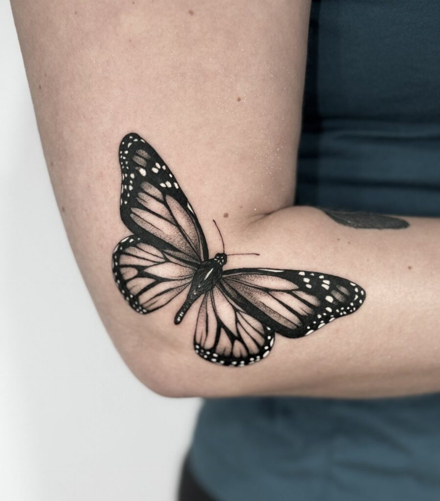 Monarch butterfly tattoo in black ink on a person's inner elbow area.