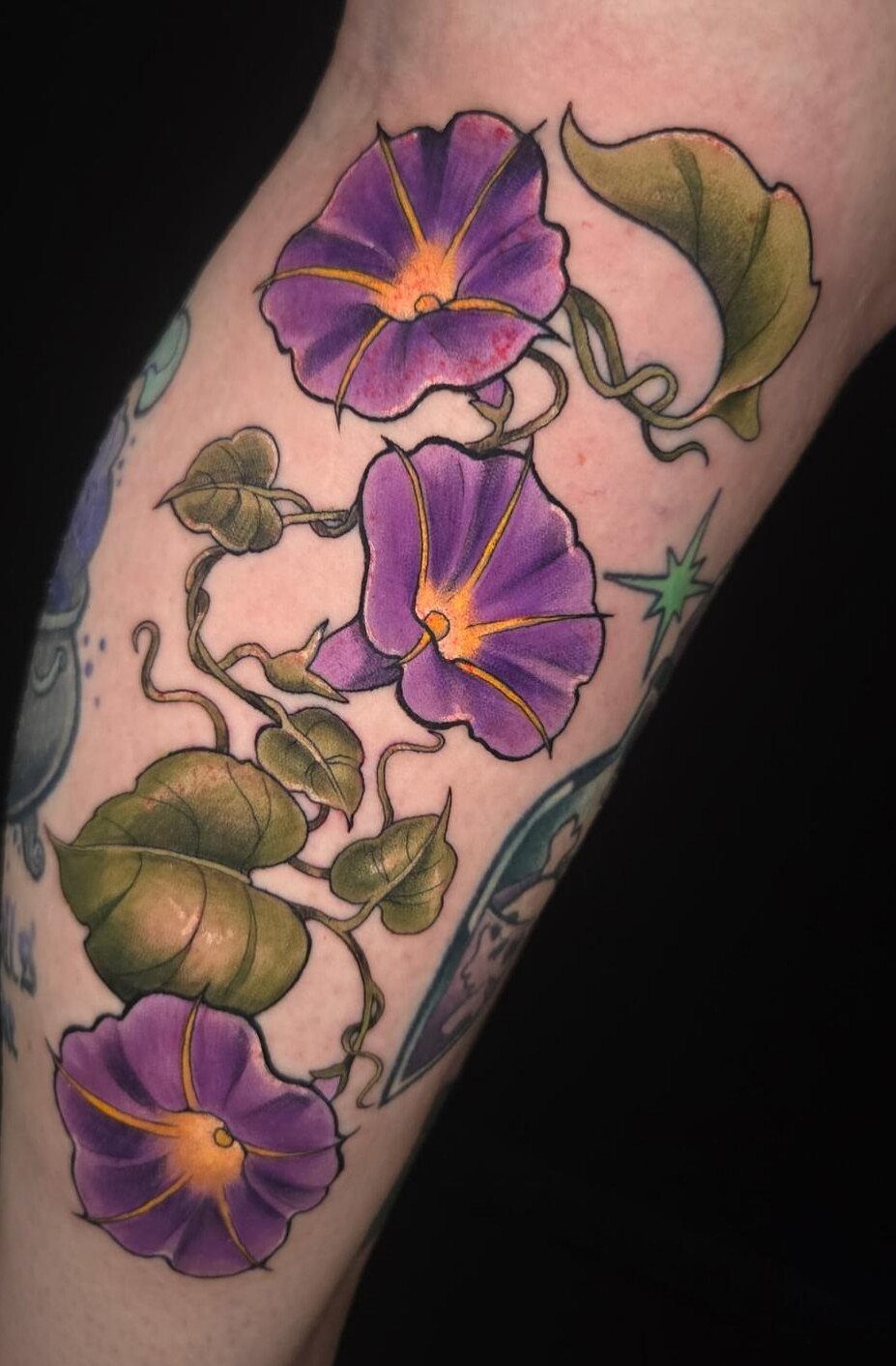 Purple morning glory flower tattoo with green leaves on a person's arm