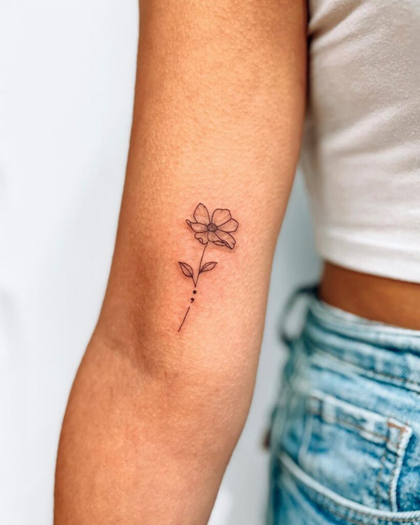 Minimalist black ink flower tattoo on a person's upper arm with dotted stem.