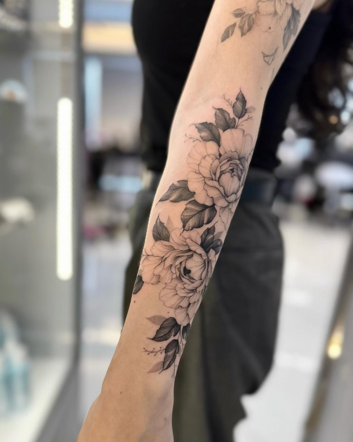 Detailed black and grey peony flower tattoo on a person's forearm.