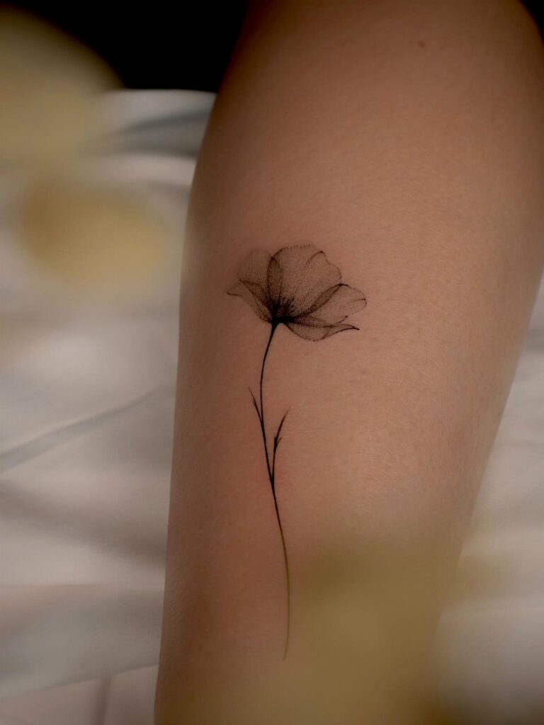 Fine line black ink poppy flower tattoo on a person's forearm