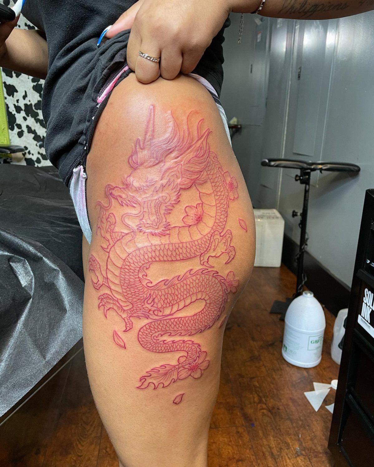 Red dragon tattoo on a person's thigh in a tattoo studio setting