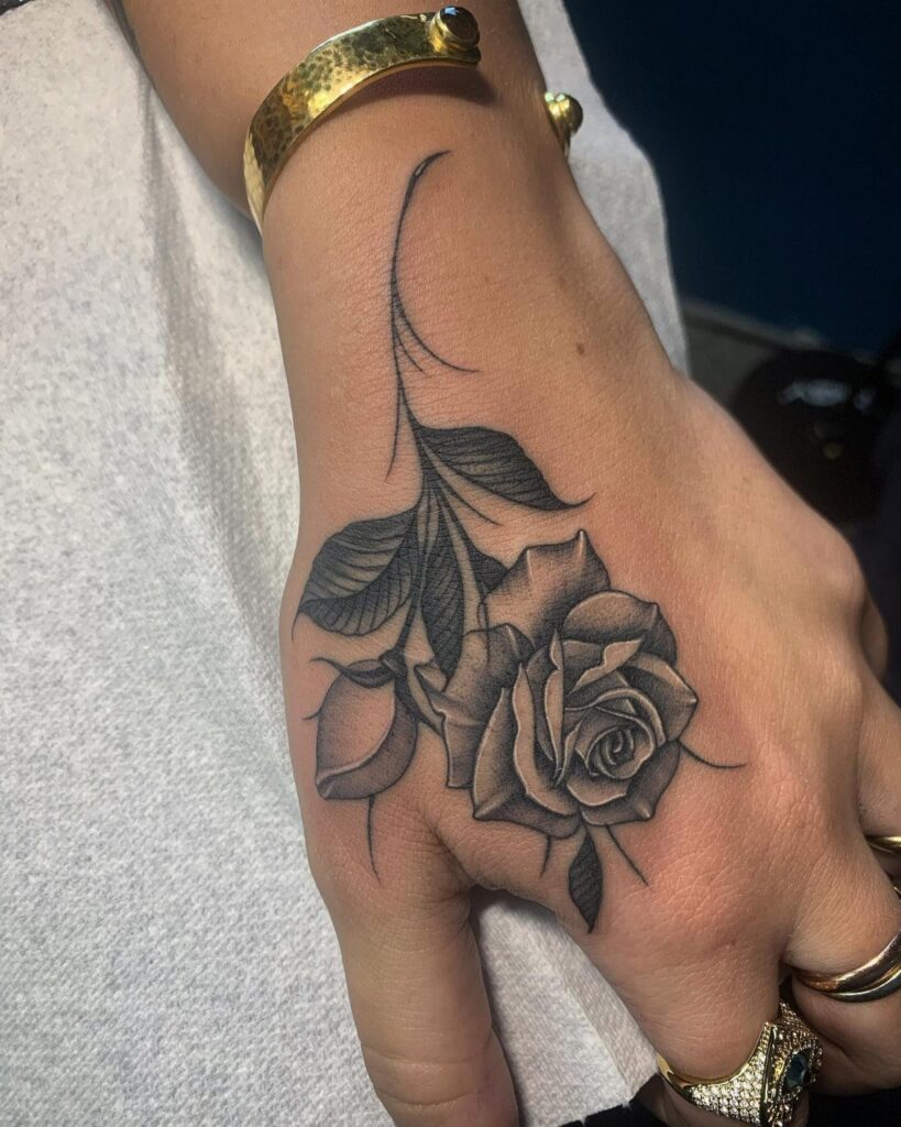 Single rose tattoo with leaves and stem on the back of a hand.