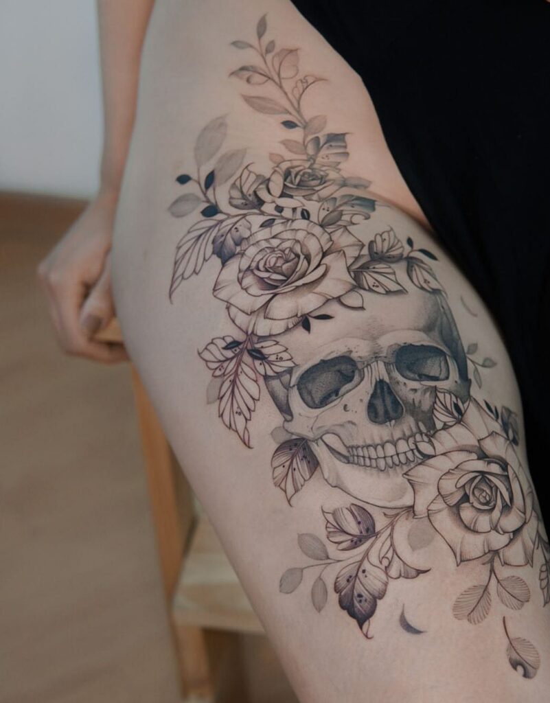 Skull and rose tattoo in black and grey ink on a person's thigh