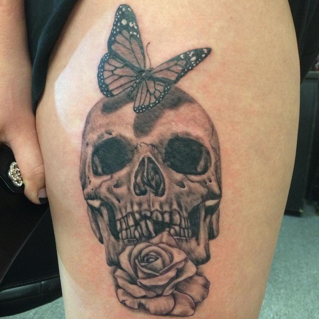 Tattoo of a shaded skull with a rose and a monarch butterfly on skin