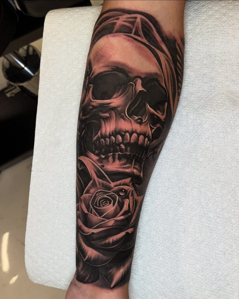 Black and grey tattoo of a skull and rose on a forearm