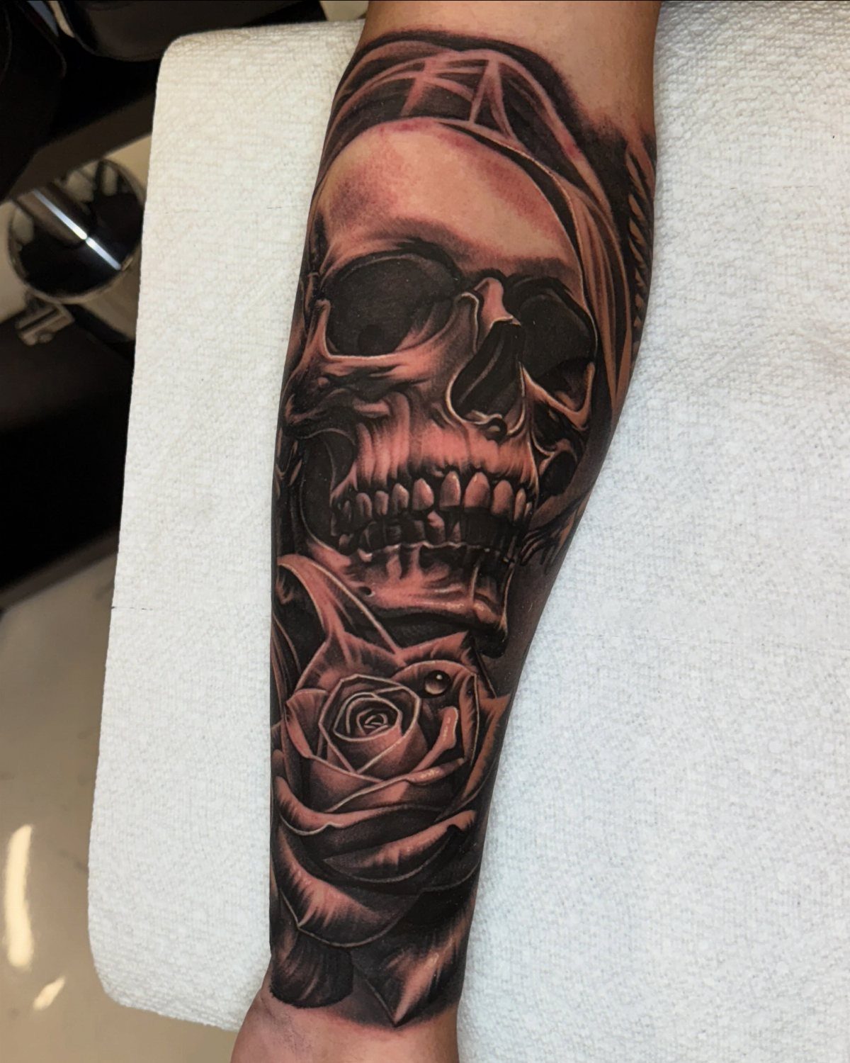 Black and grey tattoo of a skull and rose on a forearm