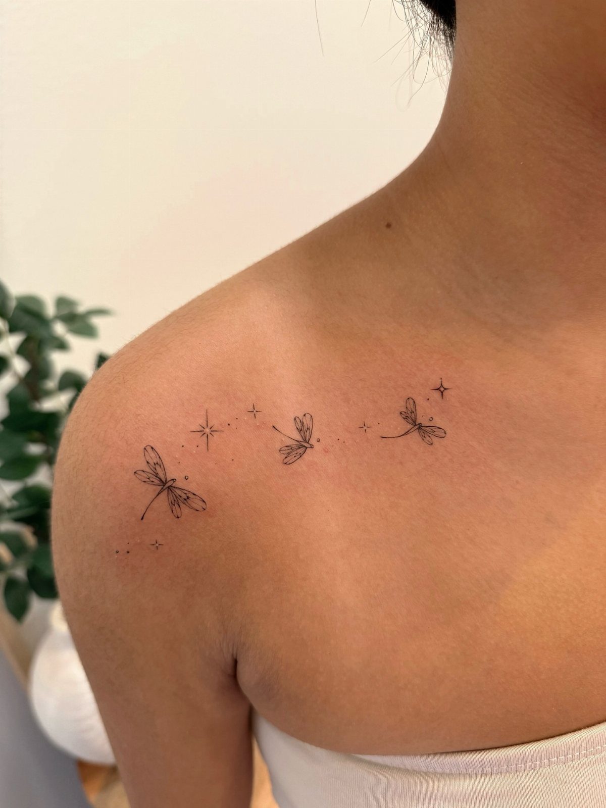 Three small dragonfly tattoos with stars on a person's shoulder and upper back.