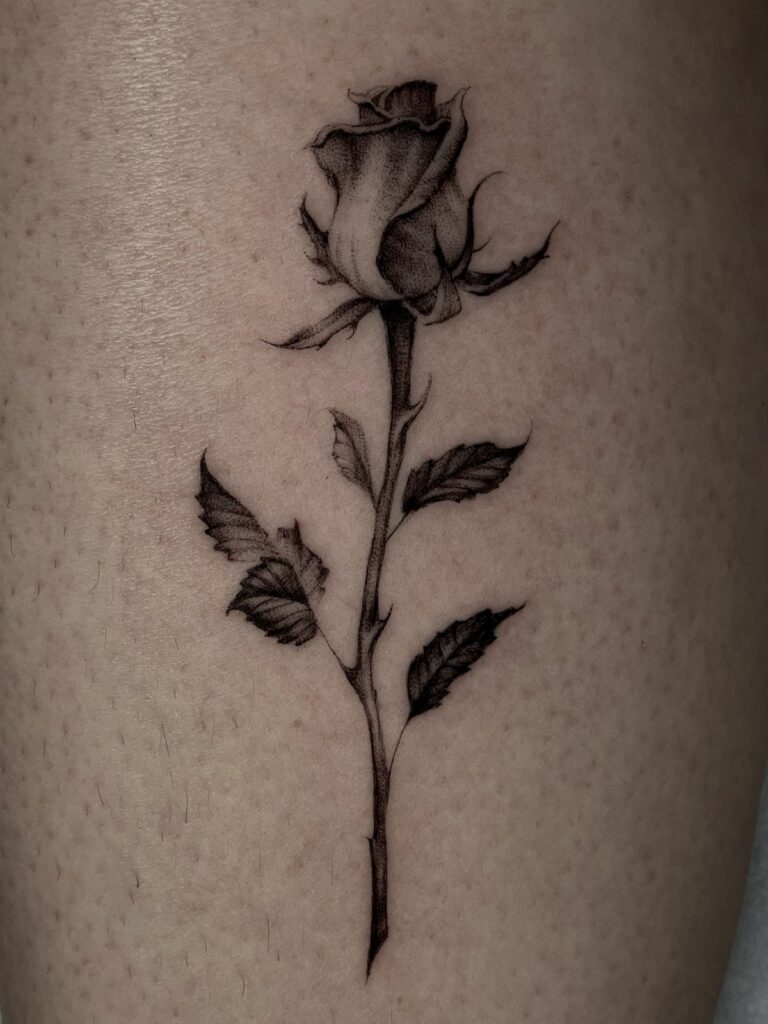 Small black and grey rose tattoo with stem and leaves on fair skin