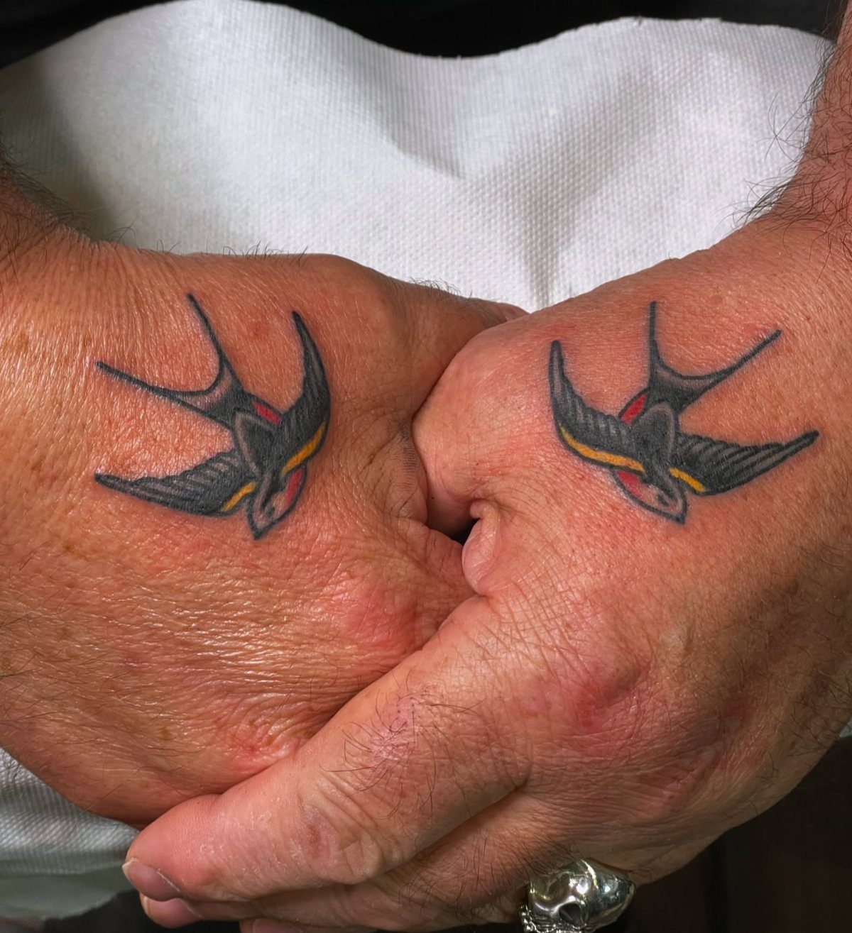 Two hands with matching traditional swallow bird tattoos on the back of each hand.