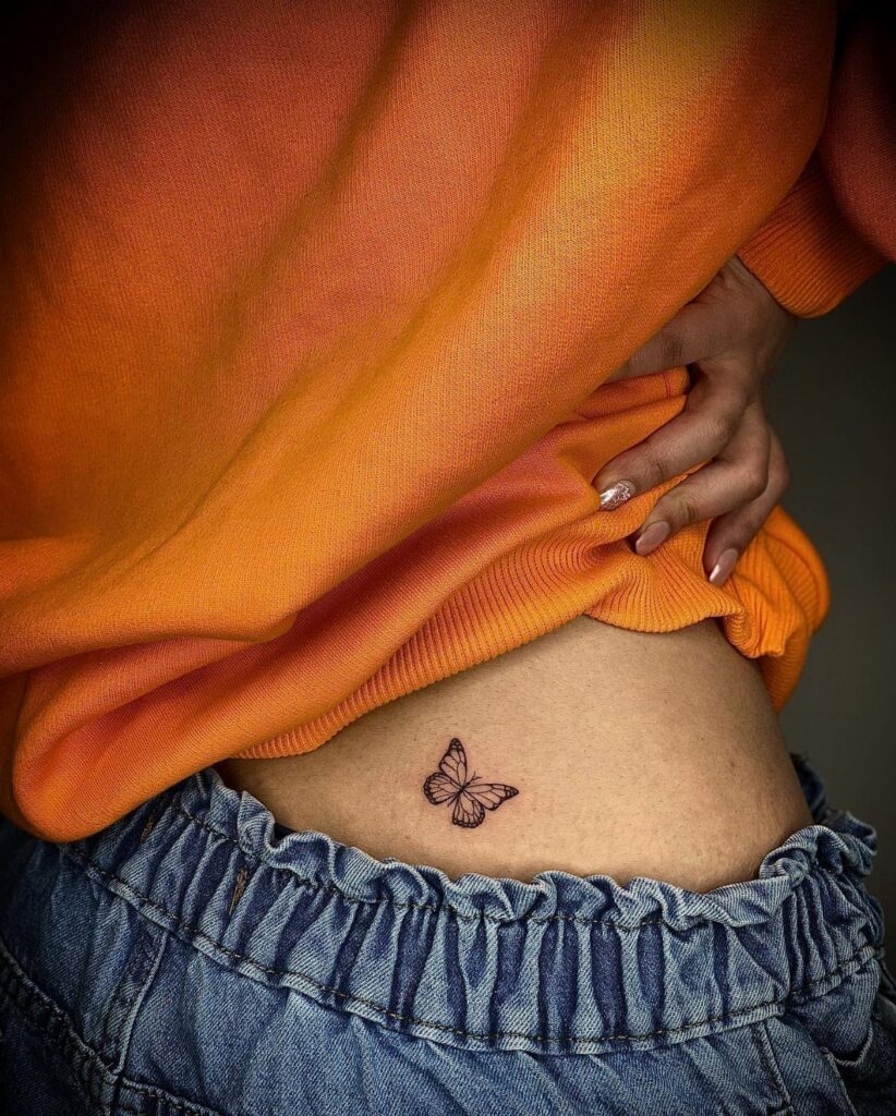 Small black butterfly tattoo on a person's lower back above blue jeans
