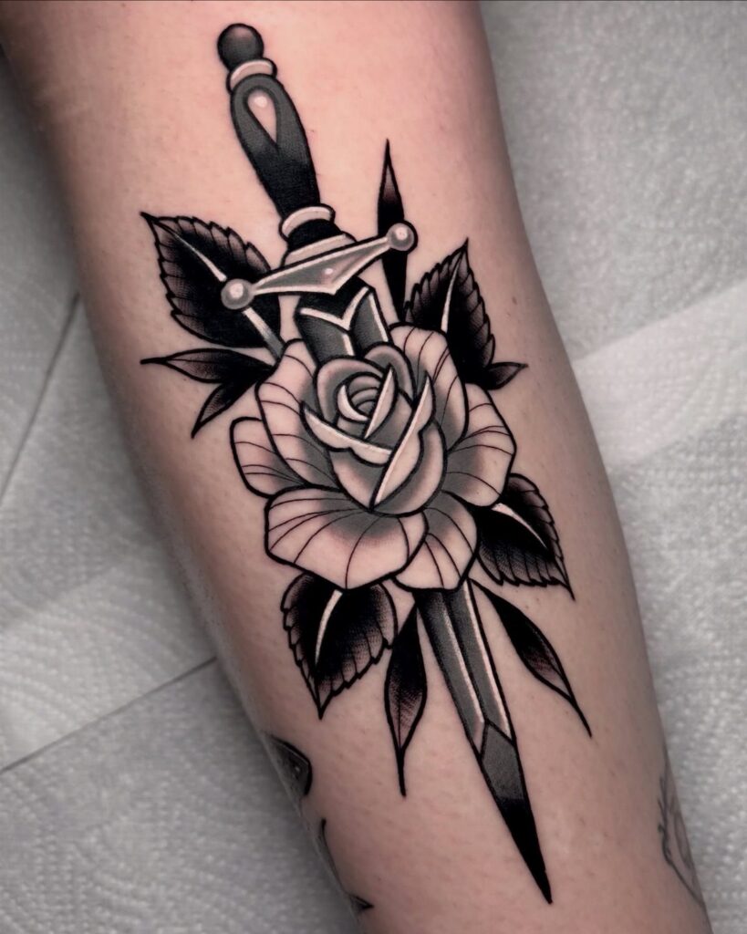 Traditional black and grey tattoo of a rose pierced by a dagger on skin