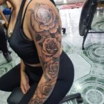 Woman with a detailed black and grey rose flower sleeve tattoo on her arm