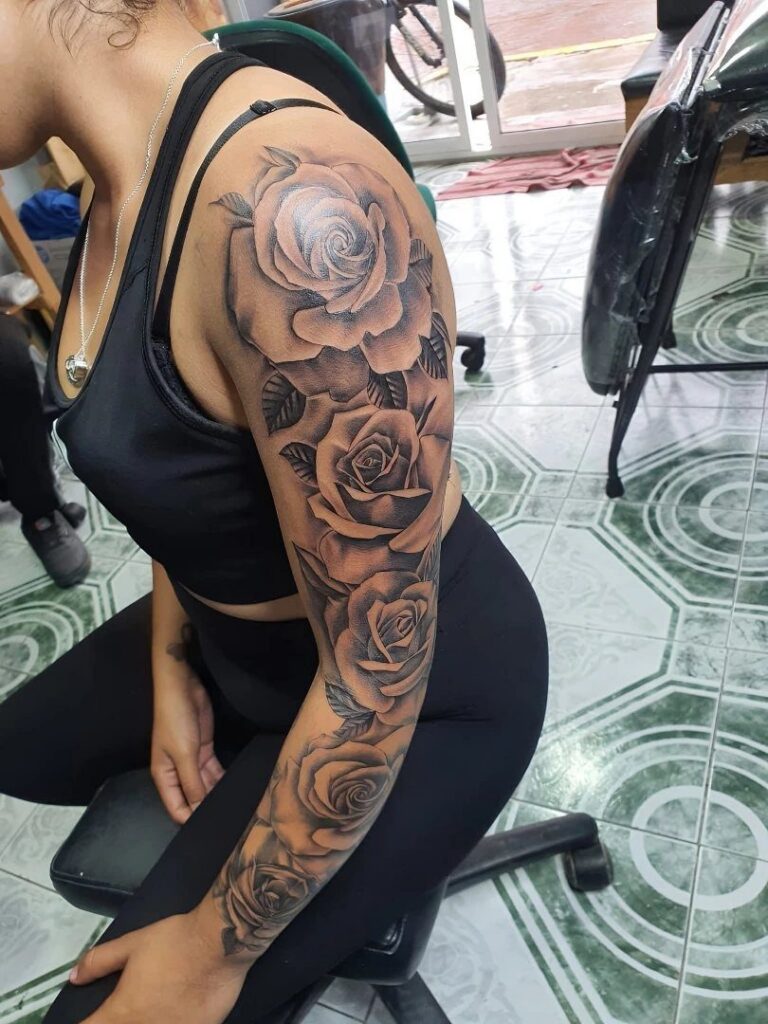 Woman with a detailed black and grey rose flower sleeve tattoo on her arm