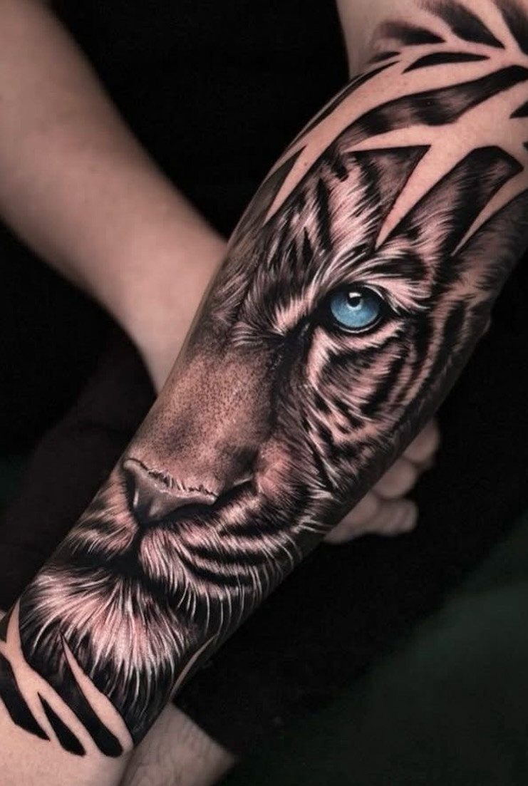 Tiger face tattoo on an arm with a vivid blue eye and detailed shading.