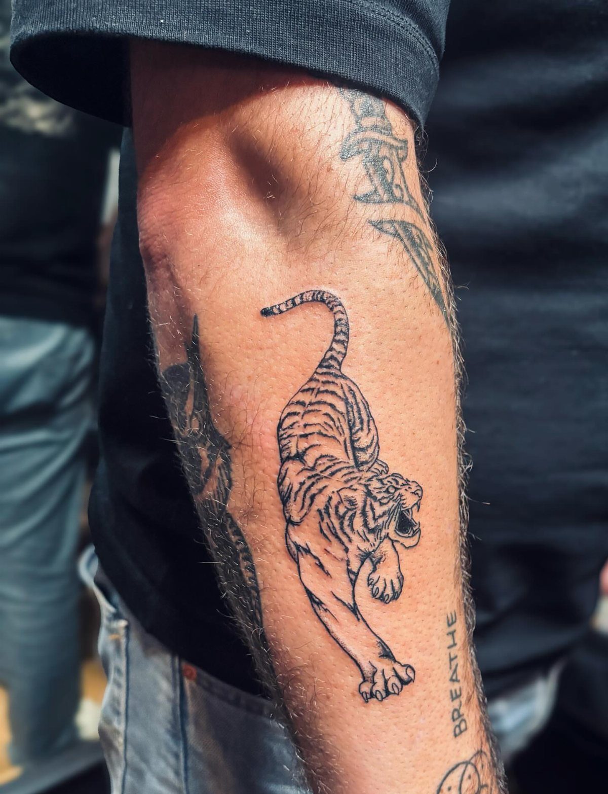 Tiger tattoo on a man's forearm showing a leaping tiger in black ink.