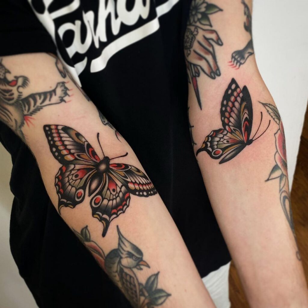 Traditional butterfly tattoos with bold outlines and red colors on a person's forearms.